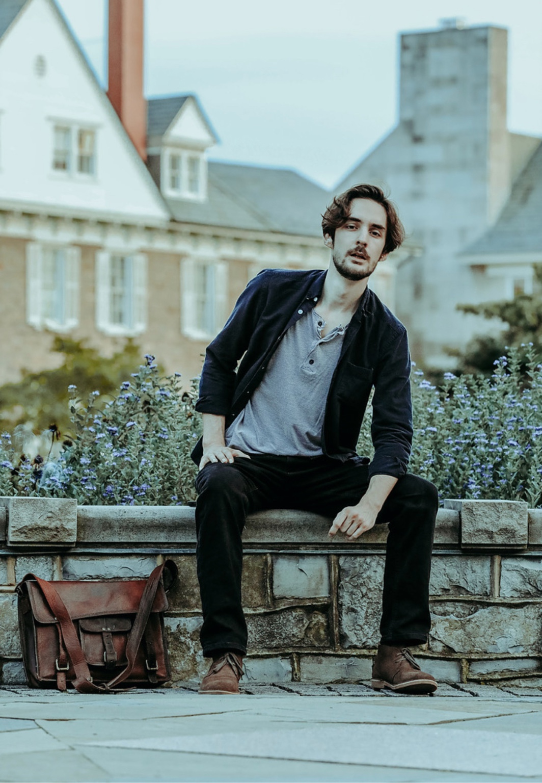 Man seated beside a garden bed with a leather satchel nearby